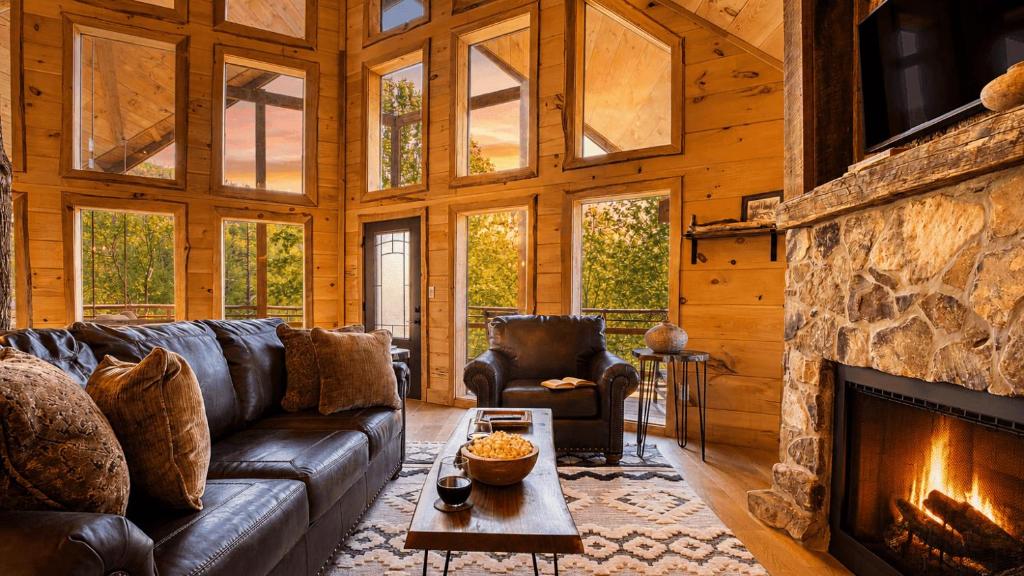 Leather sofas facing a stone fireplace and a wall of windows · © Birch Lodge