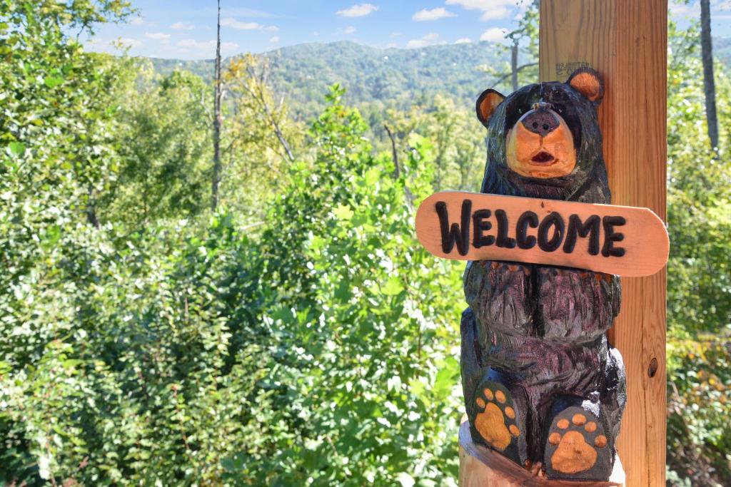 A carved bear welcomes you, with wooded ridges behind · © Cabin In The Smokeys