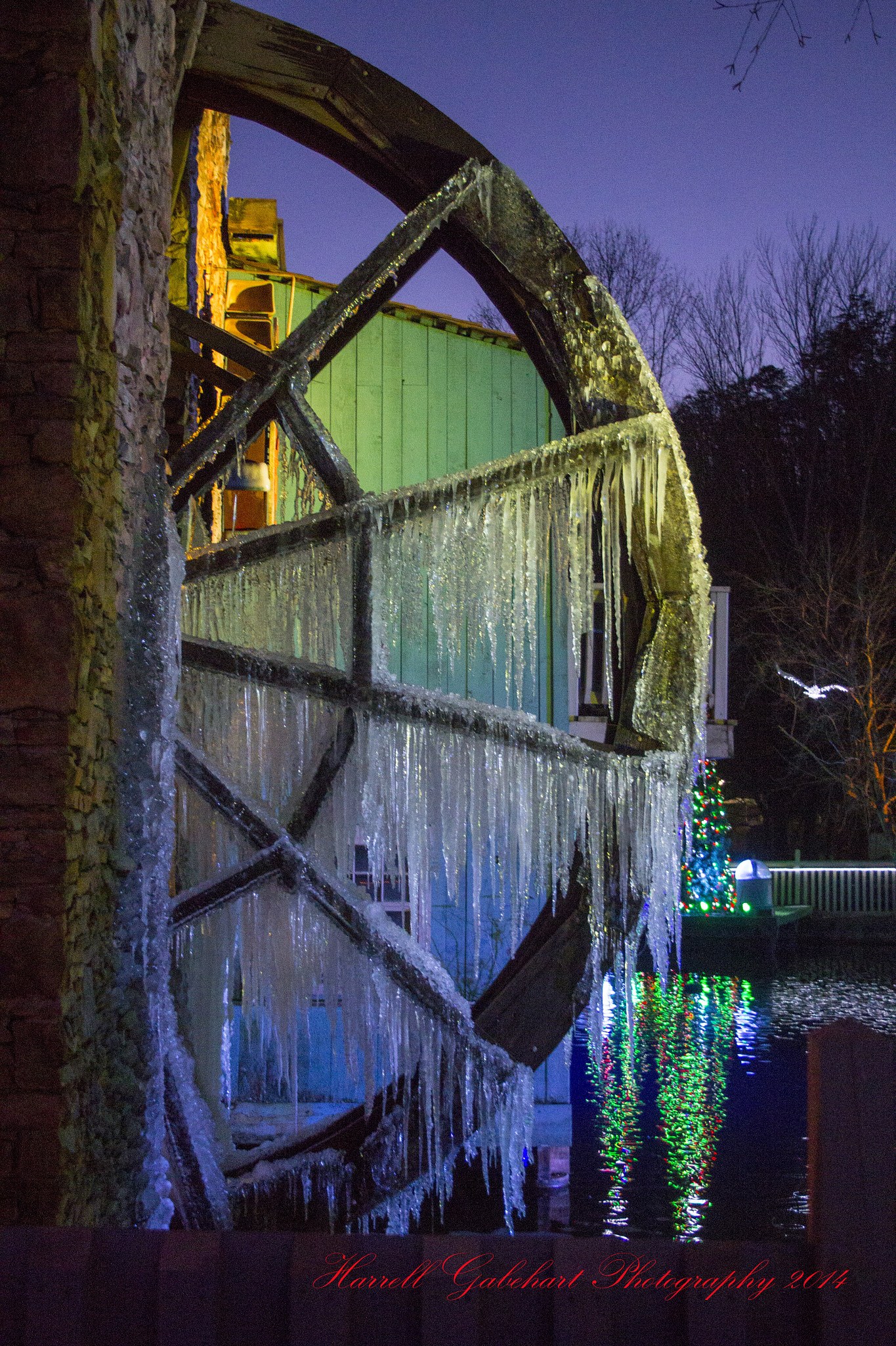 Christmas-tree lights reflected in the pond by Dollywood's frozen water wheel, on the park's last night of the season