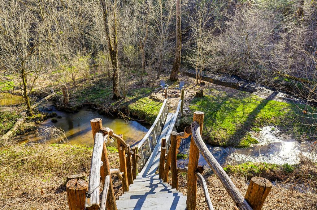 The plank footbridge crossing Caney Creek to a pair of streamside chairs · © Creekside Treehouse