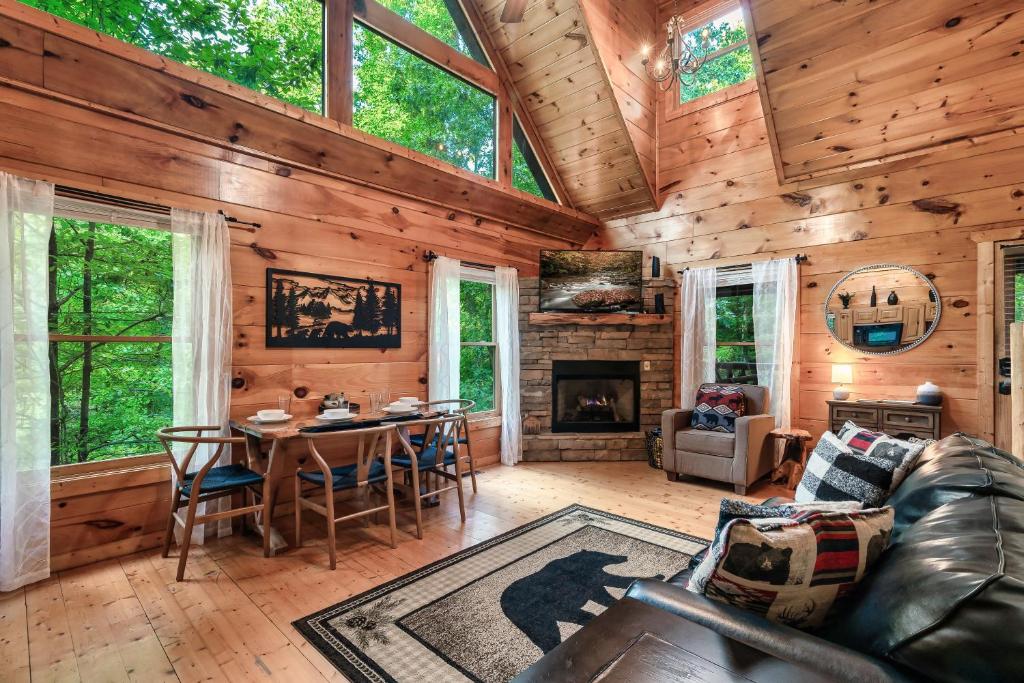 The great room, its stone fireplace and dining table under tall windows · © Ever & After Cabin