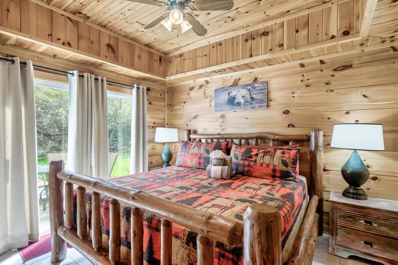 A king bed under a log frame, with the woods just past the glass · © Fireflies and Moonshine