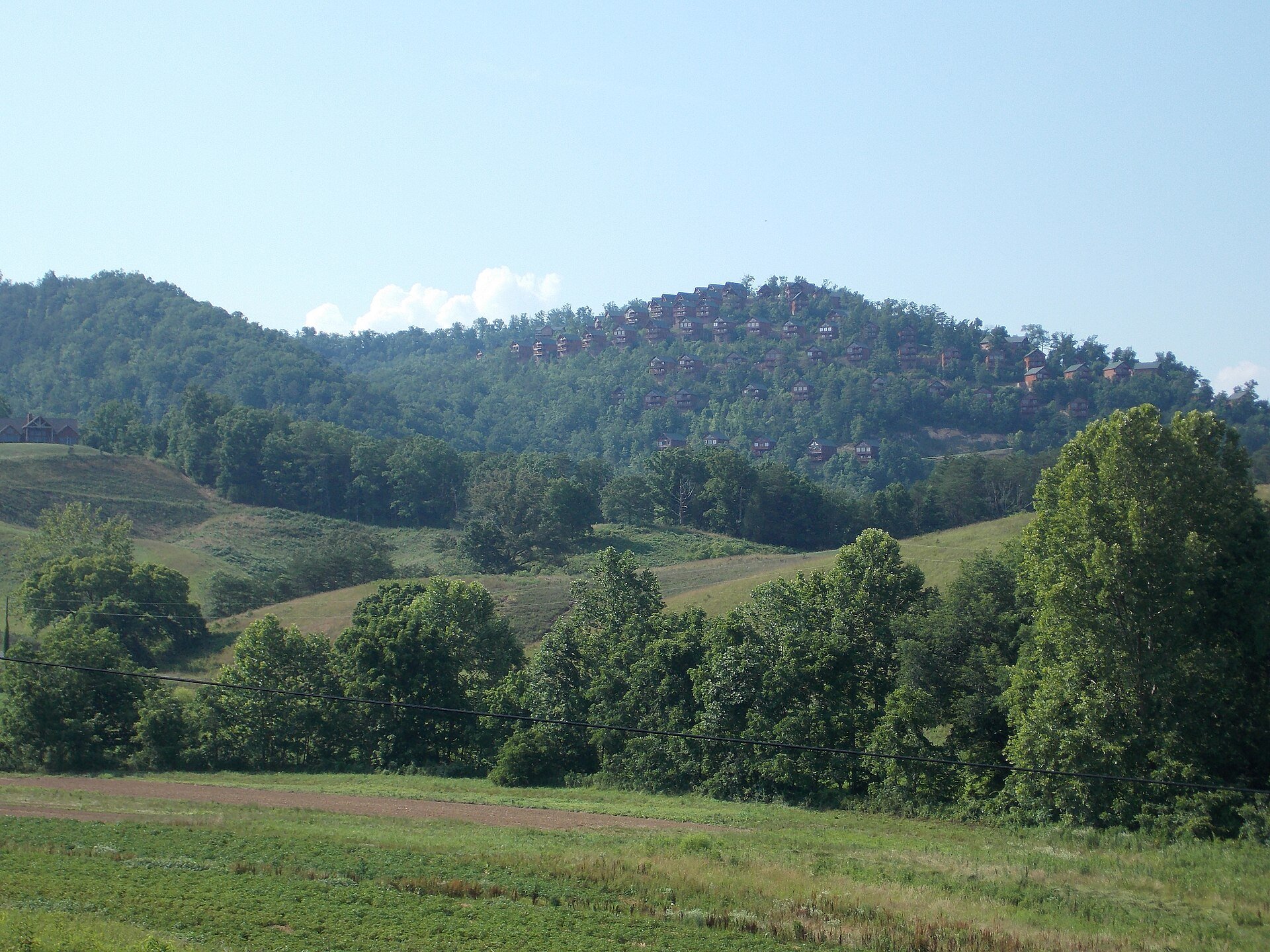 Pasture below a wooded hill of cabins, elsewhere in Sevier County
