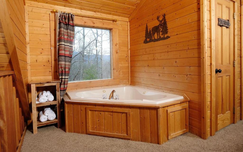 A corner jetted tub by a window onto the trees · © Knotty Escape