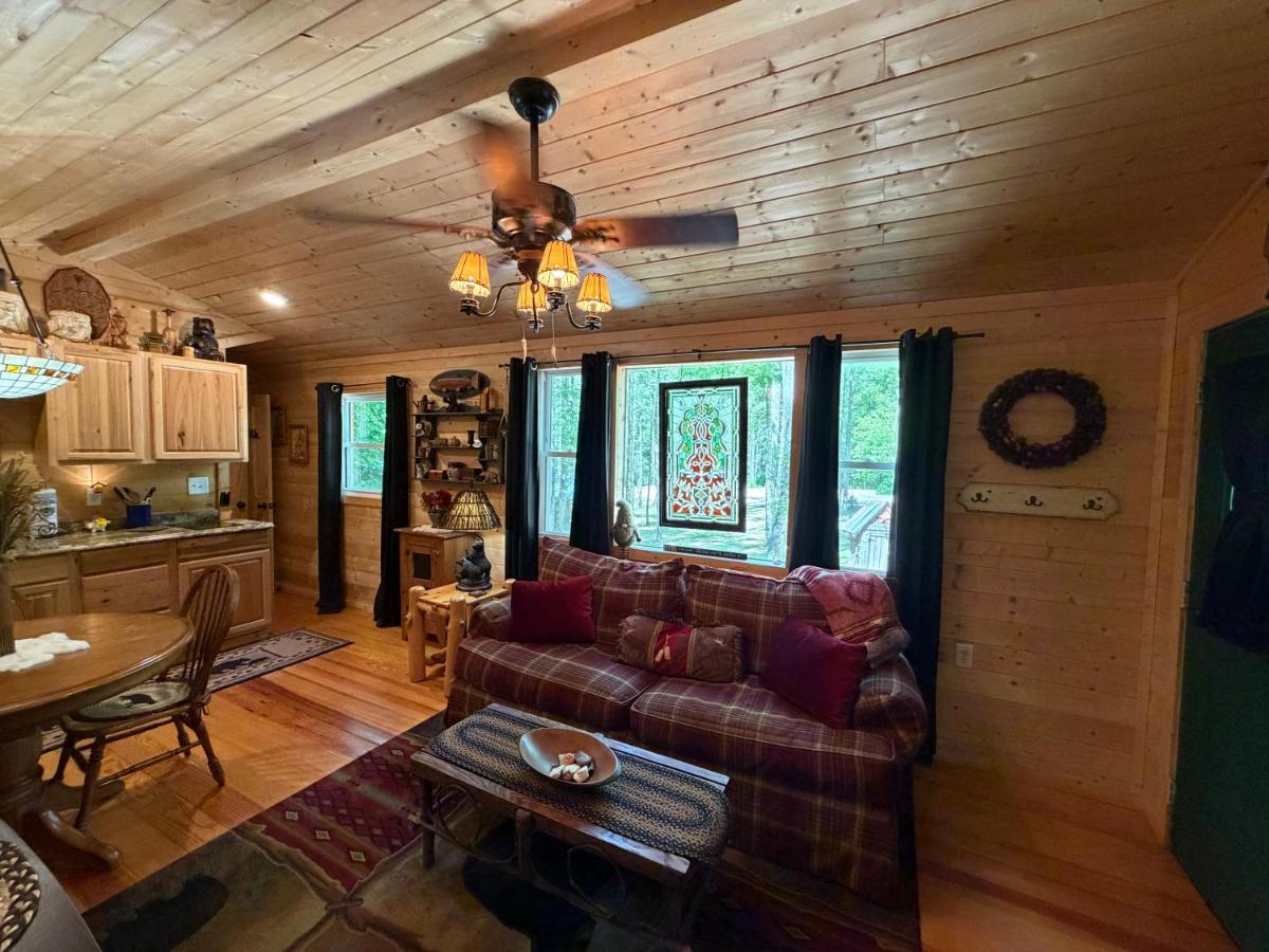 The pine living room, a plaid sofa and a stained-glass panel framing the woods · © Little Bear Tiny Cabin