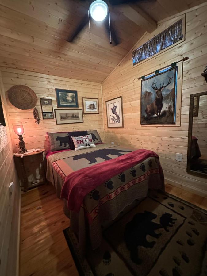 The bedroom under a black-bear quilt, lit low at night · © Little Bear Tiny Cabin