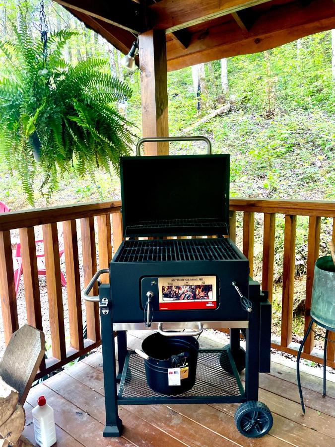 A grill on the covered deck, forest rising behind · © Little Bear Tiny Cabin