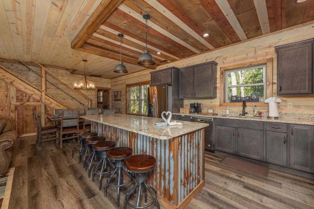 The great room with a granite island, bar stools and the stairs beyond · © Lux Cabin Mtn Views