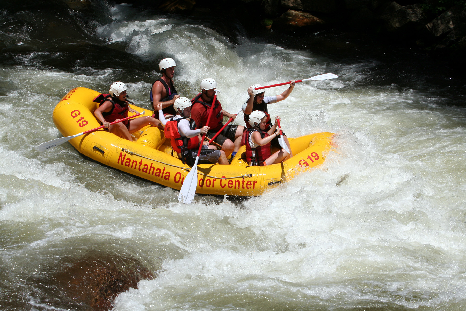 Helmeted rafters paddle an NOC raft through whitewater on the Nantahala River