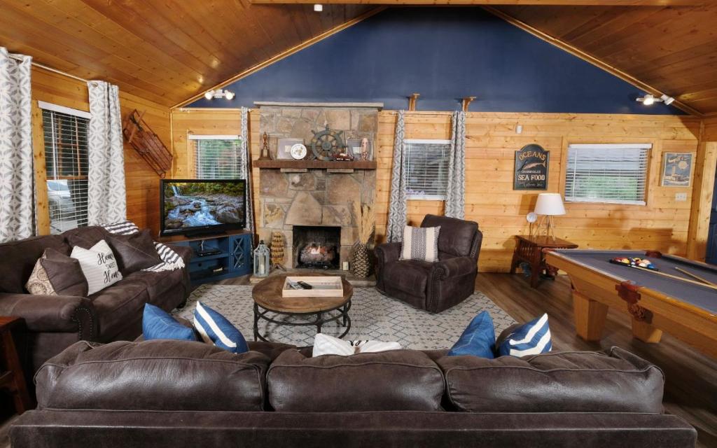 Dark sofas around the stone fireplace, with the pool table alongside · © Poolin Around