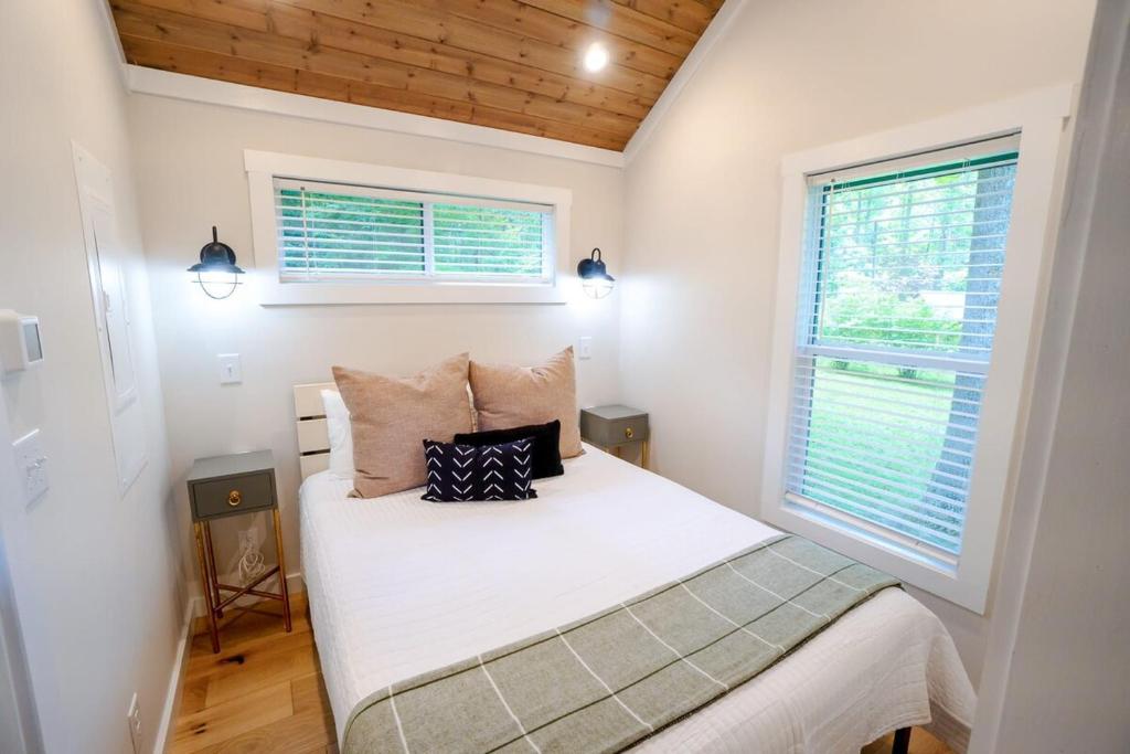 The bedroom under a timber ceiling, windows onto the woods · © Sage Cabin