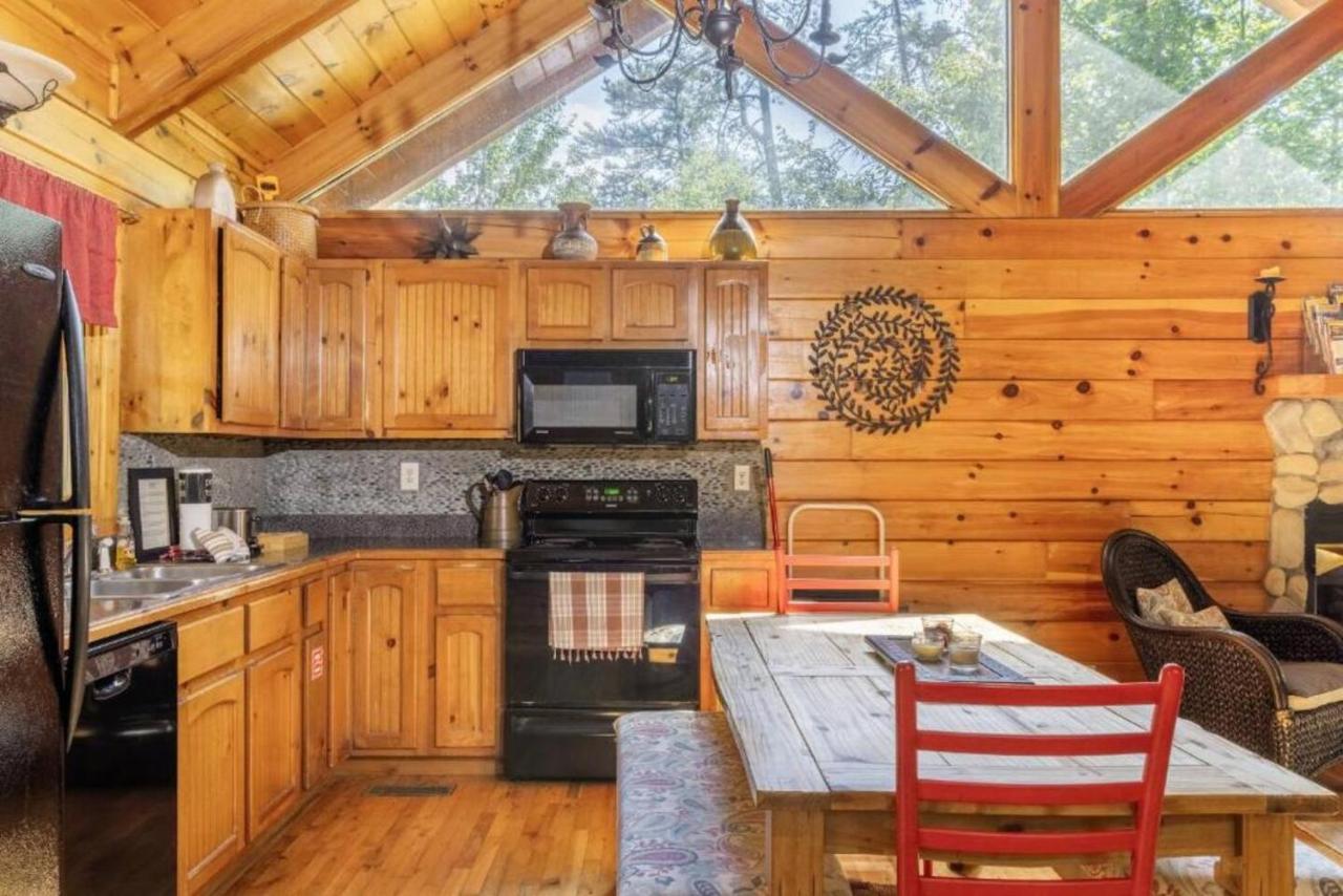 The kitchen and dining table beneath a glass gable open to the trees · © Sereni-Tree Log Cabin
