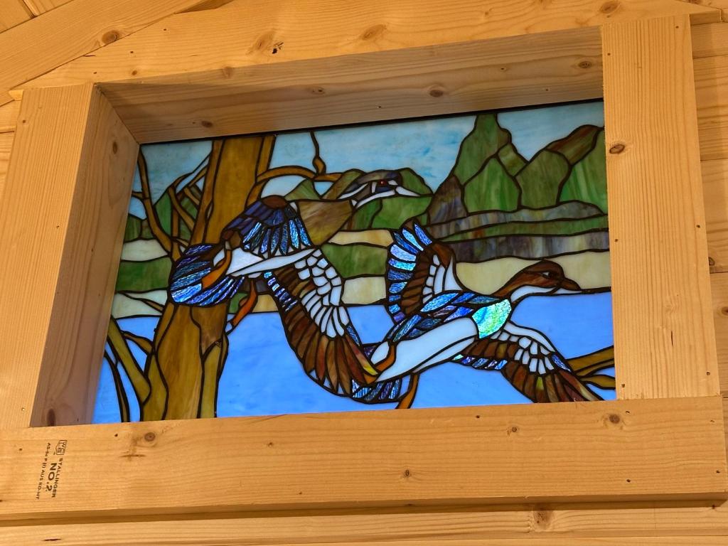 A stained-glass panel of ducks in flight over the mountains · © The Drake Cabin in The Forest