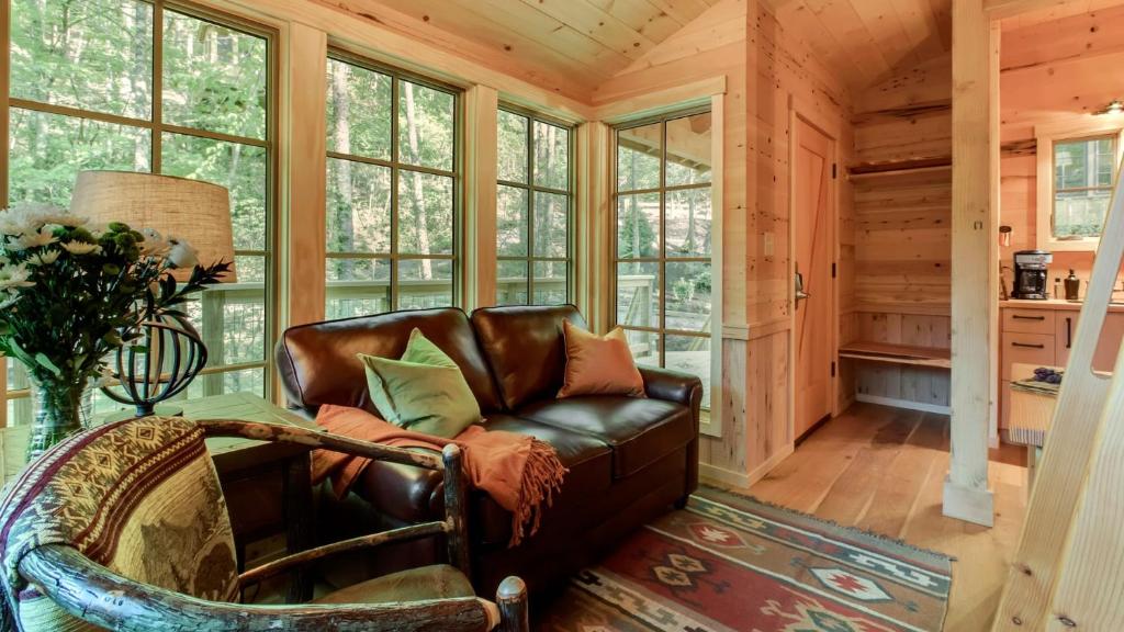 The leather sofa by tall windows onto the woods · © The Magnolia at Treehouse Grove