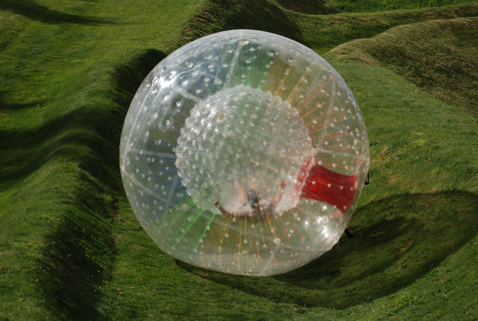 A rider in a zorb on a zig-zag grass track, location unknown